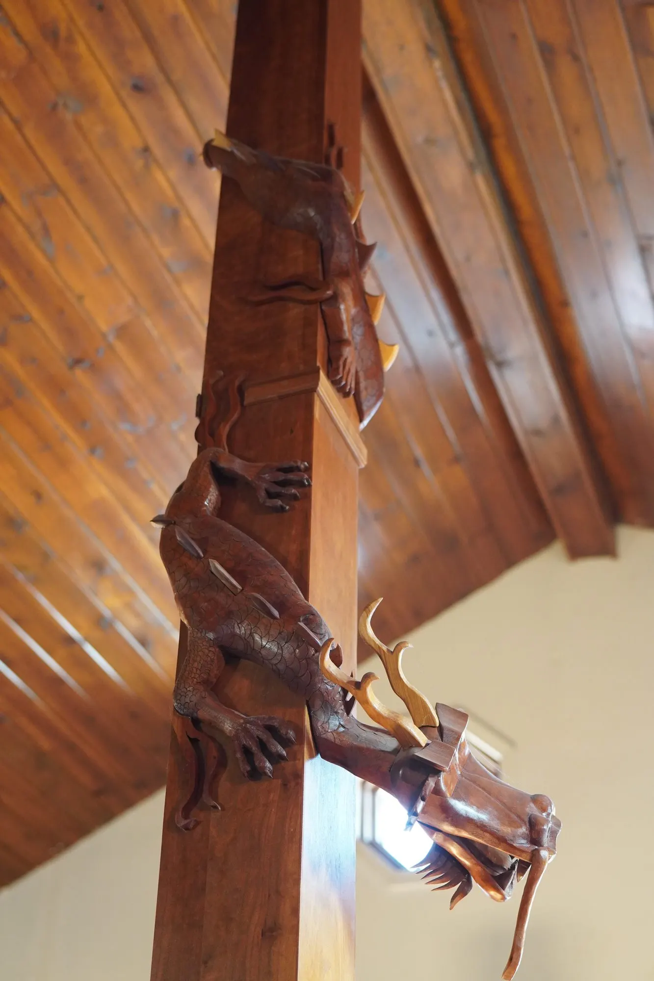 Two carved wooden dragons wrapping a square timber post beneath a wood ceiling
