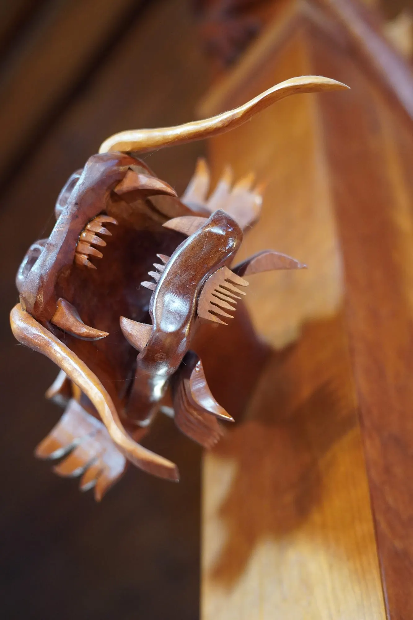 Close view of a carved wooden dragon mouth holding a fish, with teeth and whiskers in relief